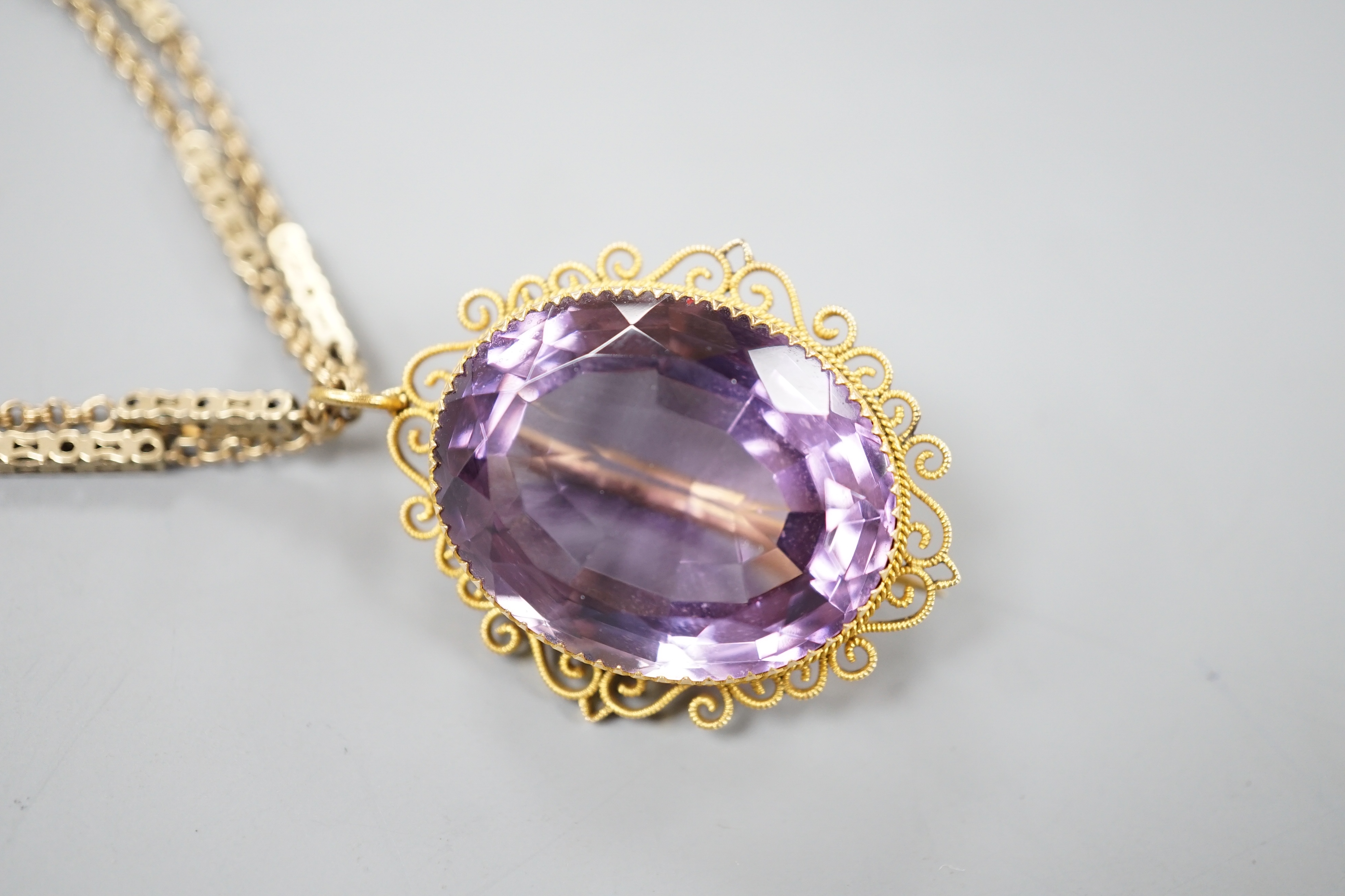 A yellow metal mounted oval cut amethyst pendant brooch, 34mm, gross 13.2 grams, on a Victorian pinchbeck guard chain, 70cm.